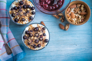 yogurt parfait with jam, nuts and berries in a glass on a rustic wooden background - top view
