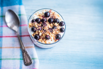 yogurt parfait with jam, nuts and berries in a glass on a rustic wooden background - top view