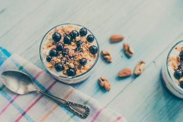 yogurt parfait with jam, nuts and berries in a glass on a rustic wooden background - top view