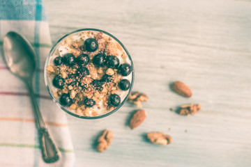 yogurt parfait with jam, nuts and berries in a glass on a rustic wooden background - top view