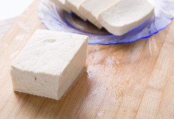 Tofu piece and cubes on chopping board.  Closeup.