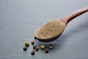 Closeup black pepper whole in wooden spoon on black stone table