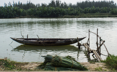 fishing boat tied up to a pier made by tying wooden poles  together on river 