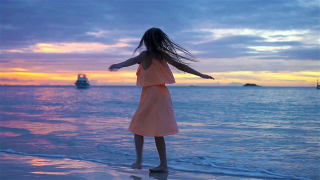 Sihouette of little girl dancing on the beach at sunset.