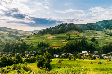 Naklejka premium Countryside rural nature landscape in summer sunny day. Discover Ukraine. Village in Carpathians mountains. Beautiful scenic view at green hills and rustic terrain. Farmer houses in forest territory.