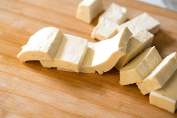Cutting tofu made of soy beans on wooden board. Tofu is mainly used in Asian and vegetarian cooking.