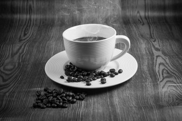 Hot coffee in white cup with coffee beans on wooden floor.