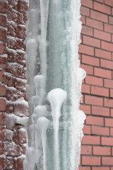Close up of drainpipe of the building covered with a thick layer of ice and icicles/ ice stalactite hanging from roof/ Poor thermal insulation of the roof leads to the formation of icicles/ 