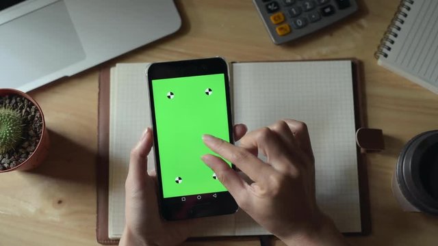 Top view of woman hand slide smartphone with green screen.
