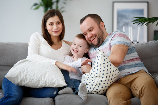 Image of happy pregnant woman, man with son on gray sofa