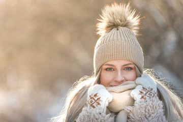 Close portrait of young caucasian woman with long hair in beige hat with fur pompon, scarf, coat, white gloves at sunny winter day, / Female wrap in and holding scarf, looking at camera, copy space