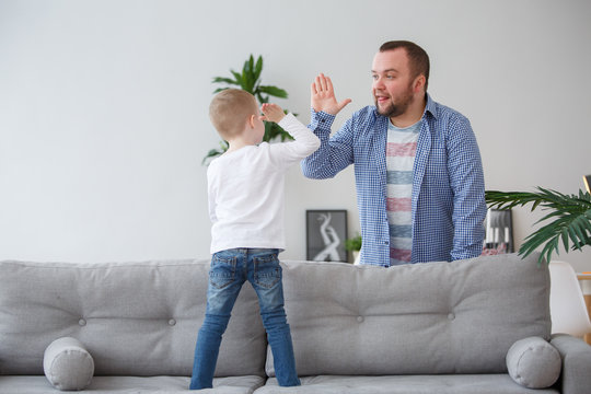 Family image of young son standing on couch doing handshake with father