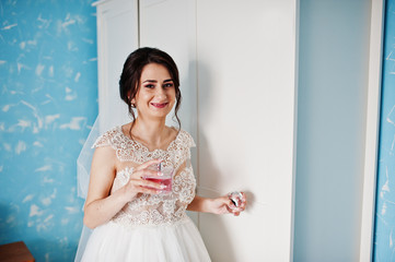 Portrait of a gorgeous bride in her room with perfumes in her hand.