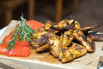 Pile of roasted grilled chicken wings on oak wooden board.