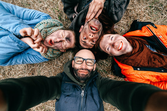 Funny selfie. Company of friends with dirty stained faces fooling around. Comic scary crazy spooky expressive faces. Group of four people lying on grass. Two men with pair of women enjoying party. - Powered by Adobe