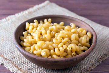 Raw macaroni in a bowl on a wooden table