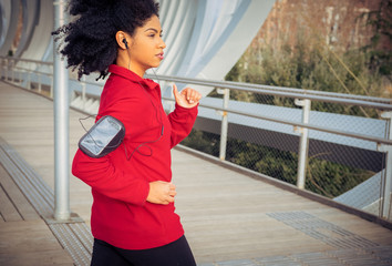 Beautiful athlete woman running with earphones, smart watch and mobile app in the park