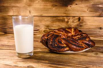 Ceramic plate with poppy seed bun and a glass of milk on wooden table