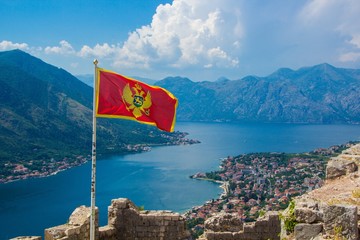 Beautiful view from above on the Kotor and Bay of Kotor, Montenegro. Waving in the wind flag of Montenegro on Ancient fortress wall above Kotor. - obrazy, fototapety, plakaty