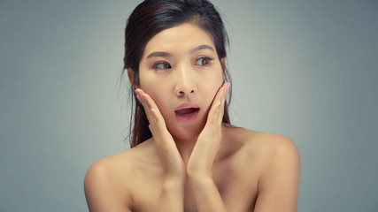 Happy beautiful asian girl with the fresh skin in grey colour background. Expressive facial expressions. Cosmetology and Spa concept.