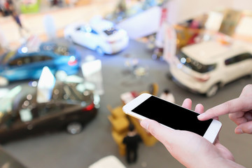Hand hold smartphone with Abstract blur car showroom top view defocused background