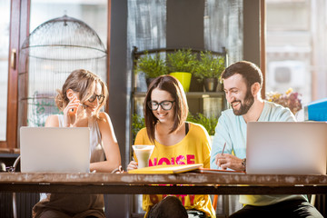 Group of caucasian coworkers dressed casually working together with documents and laptops at the big table in the beautiful cafe interior