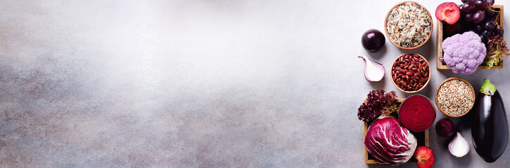 Purple vegetables, fruits on grey background. Violet eggplant, beets, cauliflower, purple beans, plums, onion, grape, quinoa, rice. Ingredients for cooking, copy space, top view, flat lay. Banner