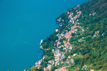 Fototapeta na wymiar Small beautiful European town on the shore of the lake. Como lake top view. Lombardy, Italy. The beautiful landscape of the lake and a small European town with red-tiled roofs.