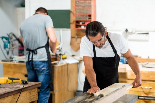Carpenter using table saw for cutting wood at workbench