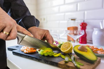 The man is cutting the ingredients for shrimp and avocado salad.