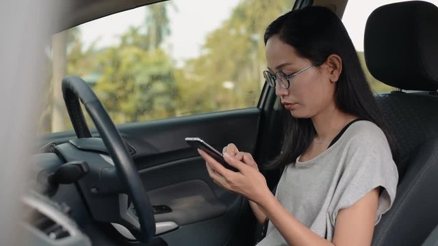 
Asian woman sits in the car and works on smartphone.