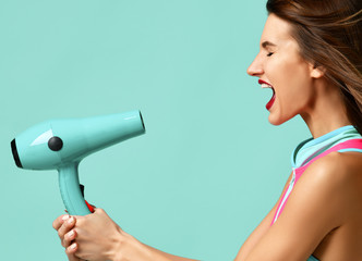 Happy young brunette woman with hair dryer on blue mint background