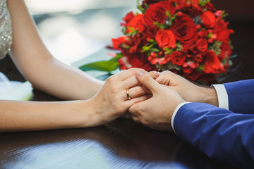 Obraz na płótnie Canvas Hands of couple on a table with a wedding bouquet