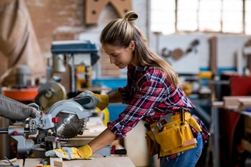 Female carpenter cutting wooden plank with electric saw