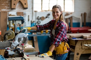 Female carpenter cutting wooden plank with electric saw 