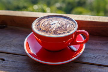 coffee in a red cup on a wooden table  in front of hill