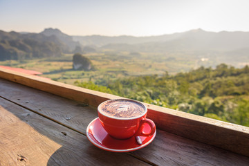 coffee in a red cup on a wooden table  in front of hill