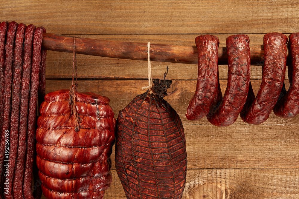 Wall mural Composition of different type of sausage hanged on wooden background