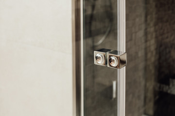 Small square ergonomic metal knob a button for a glass door to a shower stall in a monochrome minimalist bathroom interior