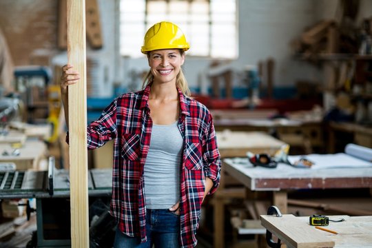 Portrait of female carpenter standing with wooden plank