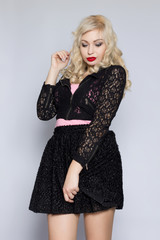 Fototapeta premium Portrait of a beautiful young blonde woman in a black lace suit. Girl posing in studio on gray background