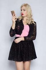 Portrait of a beautiful young blonde woman with curly hair in a black lace suit with a mobile phone in her hand