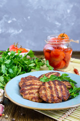 Juicy cutlets, fried on a grill in a ceramic plate and canned tomatoes on a wooden background.