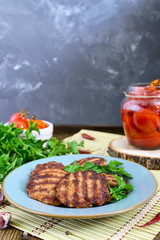Juicy cutlets, fried on a grill in a ceramic plate and canned tomatoes on a wooden background.