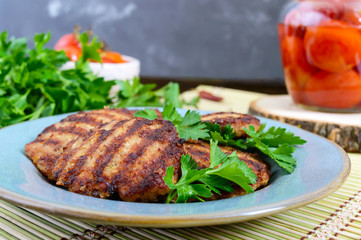 Juicy cutlets, fried on a grill in a ceramic plate and canned tomatoes on a wooden background.