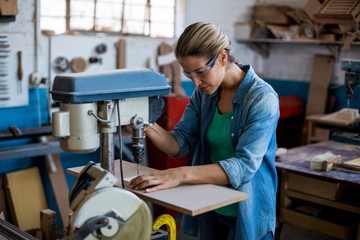 Female carpenter drilling a hole in a wooden plank