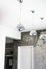 Silver pendant lamps with reflection hanging against white ceiling and gray wall backdrop. Modern white apartment design, minimalism concept