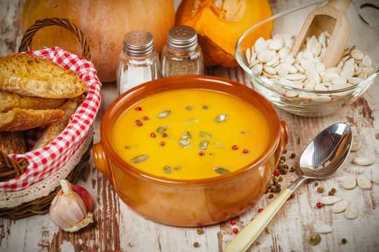 Homemade pumpkin soup in a clay bowl on rustic white table