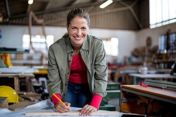 Female carpenter marking on wooden plank with pencil