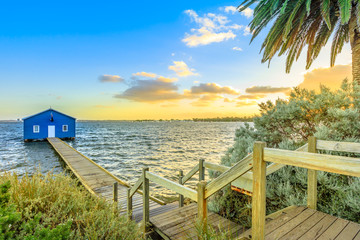 Fototapeta premium The iconic landscape of Blue Boat House or Crawley Edge Boatshed with wooden jetty on Swan River at sunset light. One of the most photographed locations in Perth, Western Australia, near Kings Park.